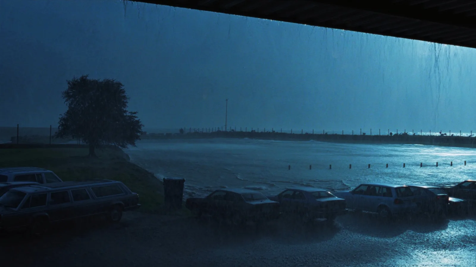 chuva forte escorrendo do telhado de um estacionamento coberto, com carros secos embaixo
