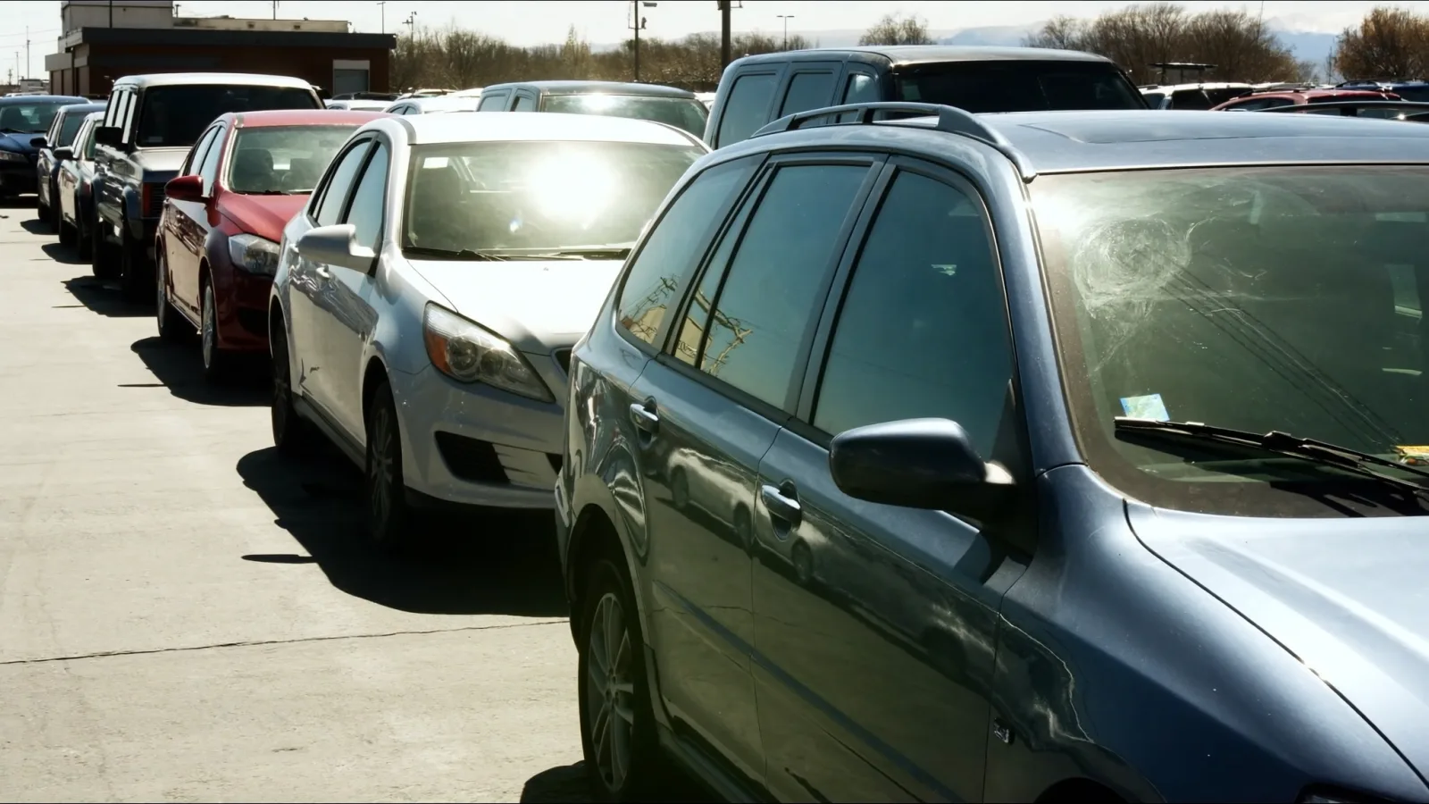 carros estacionados sob sol forte em pátio descoberto, com calor subindo do asfalto