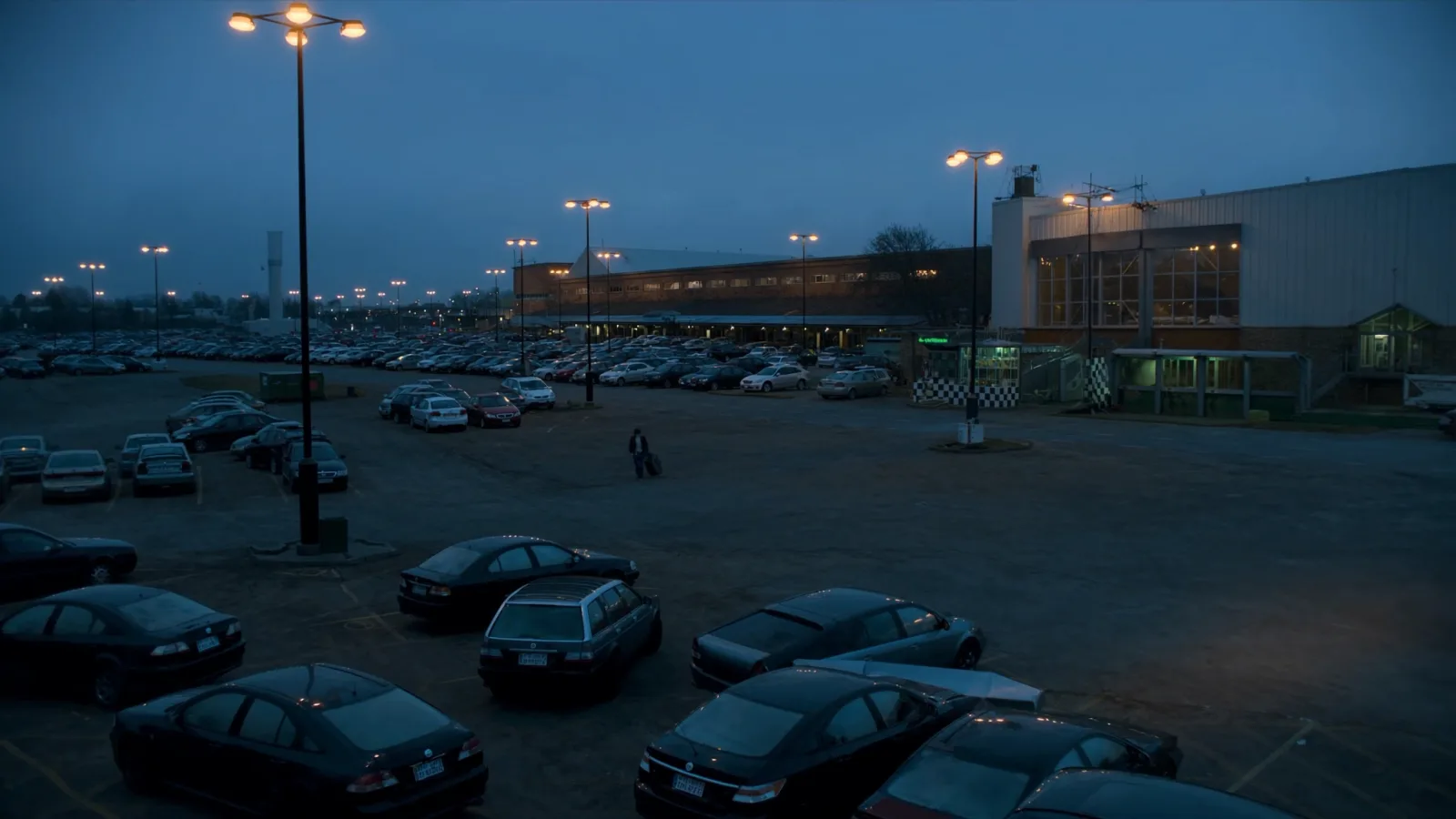 estacionamento de aeroporto na madrugada, com carros e terminal iluminado ao fundo